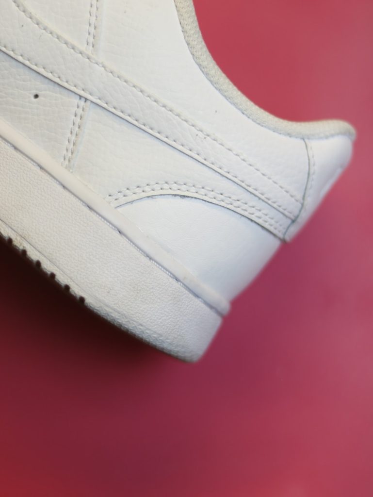 a close up of a white tennis shoe on a red surface